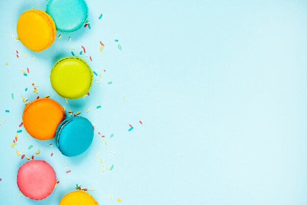 Top view of colorful macaroons and sugar sprinkles arranged on blue background.