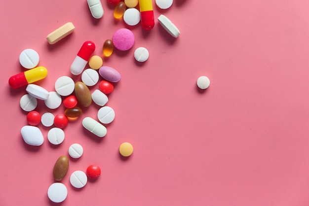 Top view of colorful pills spilling on pink background