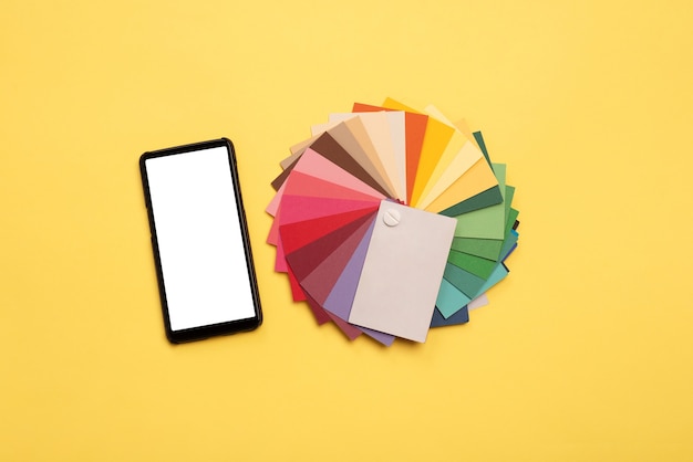 Photo top view of colorful samples and smartphone with blank screen on yellow background.