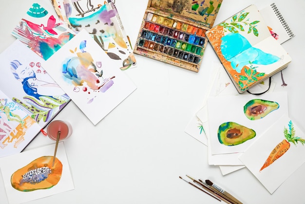 Top view of colorful watercolor paintings and drawing utensils