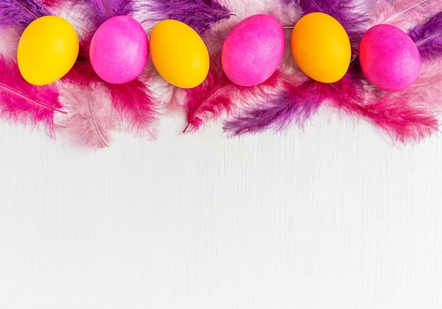 Photo top view of colourful bright pink and yellow painted easter eggs with feathers on white wooden table