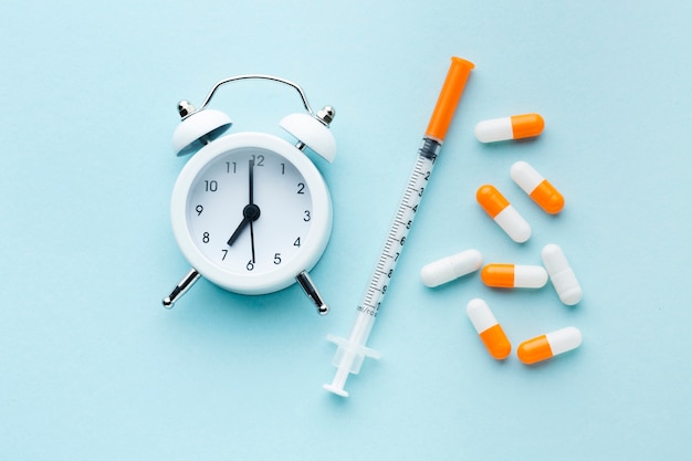 Top view colourful pills and white clock with syringe