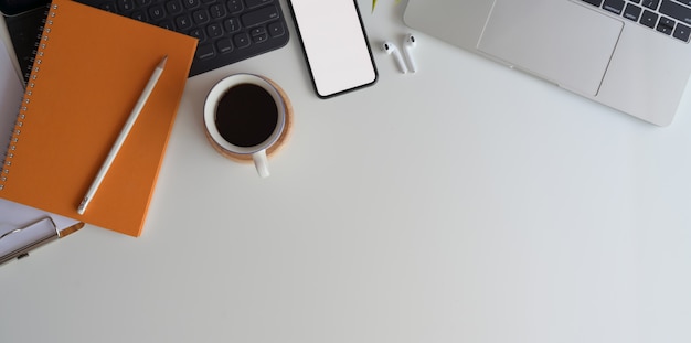 Top view of comfortable workspace with blank screen smartphone on white wooden desk with office supplies 