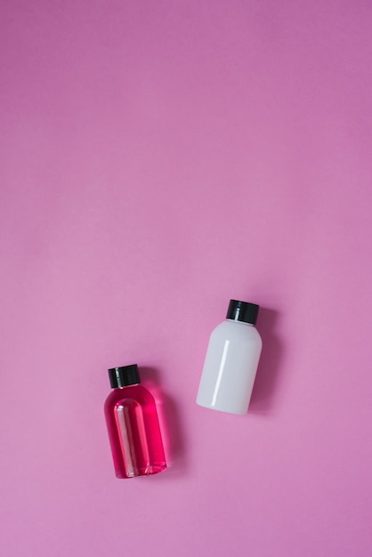 Top view composition of small travel bottles for cosmetics, shower gel, shampoo and hair balm on a pink table. Concept of body or hair skin care with copy space.