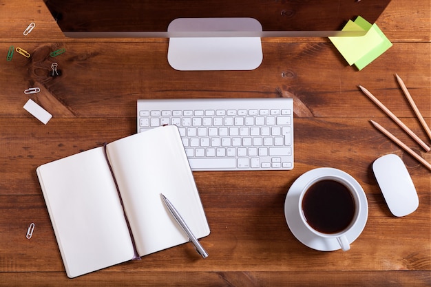 Top view of computer keyboard notebook and coffee on brown wooden table