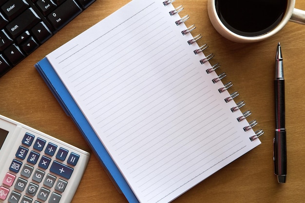 top view of computer keyboard with black coffee by calculator and diary on desk