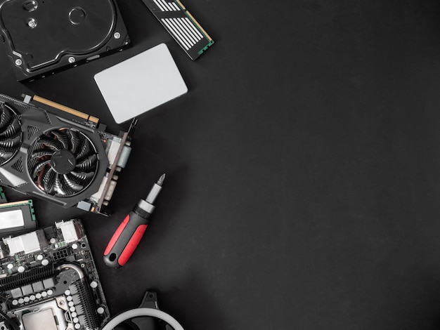 Photo top view of computer parts with harddisk, ram, cpu, graphics card, and motherboard on black table background.