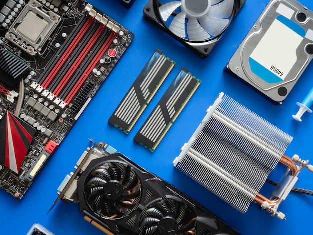 top view of computer parts with harddisk, ram, CPU, graphics card, and motherboard on blue table background.