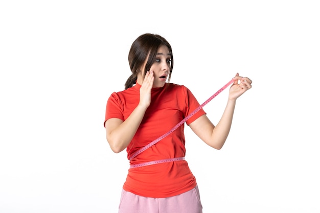 Top view of a concentrated young lady in redorange blouse and holding metre measuring her waist on white background