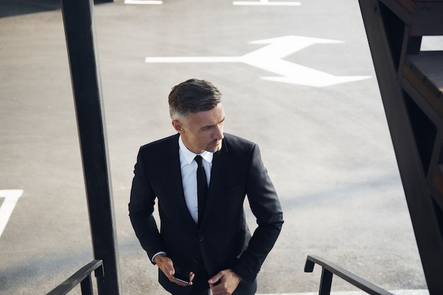 Top view of confident mature businessman carrying mobile phone while walking outdoors