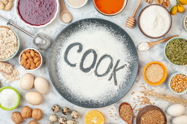 top view cook written flour with cereals eggs seeds nuts jam and jelly on the white surface