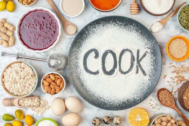 top view cook written flour with cereals eggs seeds nuts jam and jelly on white surface