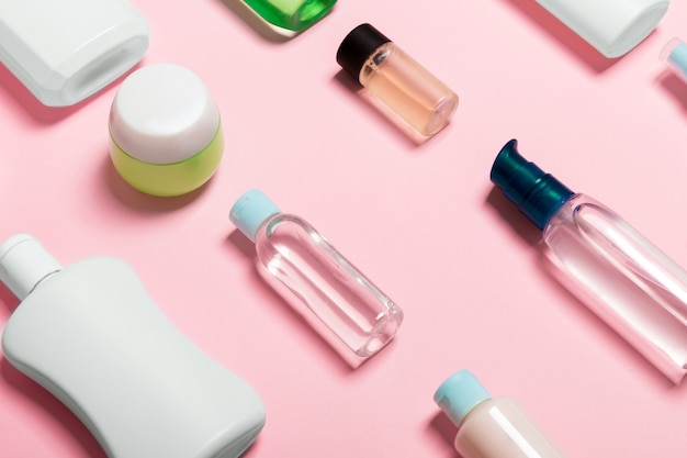 Top view of cosmetic containers, sprays, jars and bottles on pink background.