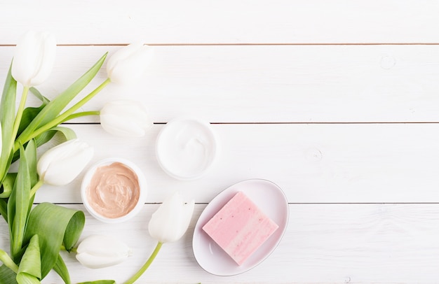 Vista dall'alto di creme cosmetiche e sapone con tulipani bianchi vista dall'alto piatto giaceva su fondo di legno bianco