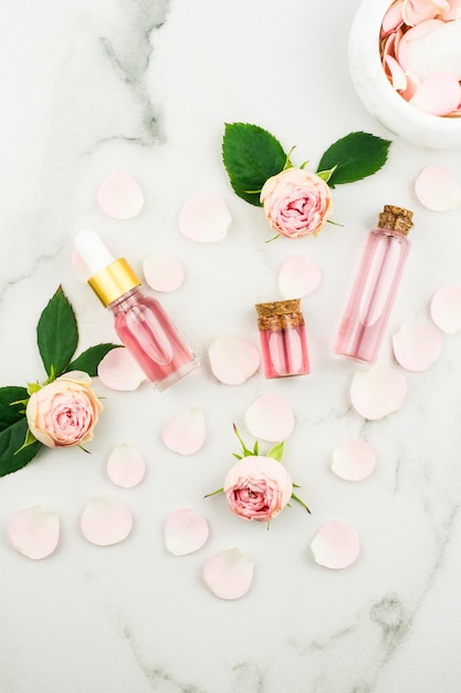 Top view of cosmetic and glass bottles with cork lid with rose water and rose essential oil white ba...