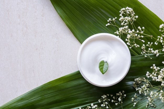 Top view of cosmetic lotion with flowers and green leaf.