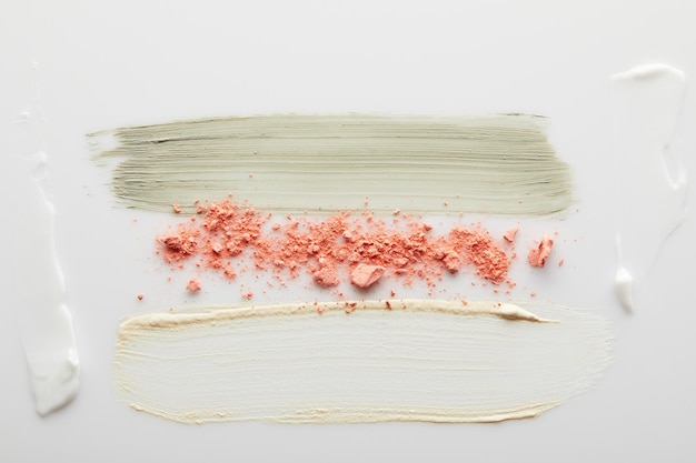 Top view of cosmetic and tone cream clay brushstrokes with blusher on grey background