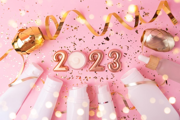 Photo top view of the cosmetics containers on pink background rose gold numbers 2023 above