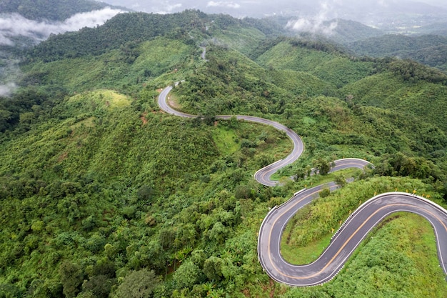 Top view of countryside road passing through the green forrest and mountain