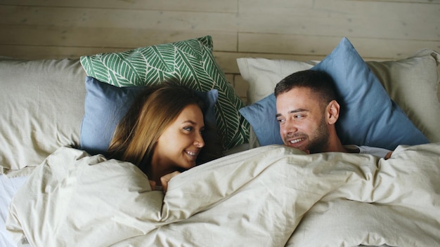 Top view of couple having fun in bed lying under blanket looking each other