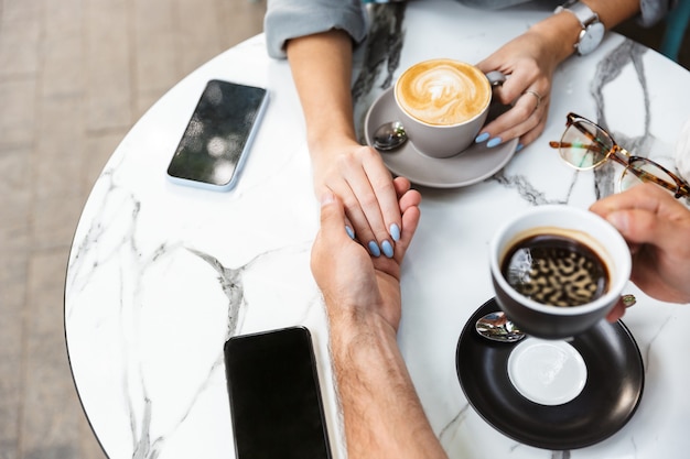 Top view of a couple in love on a date sitting at the cafe table outdoors, drinking coffee