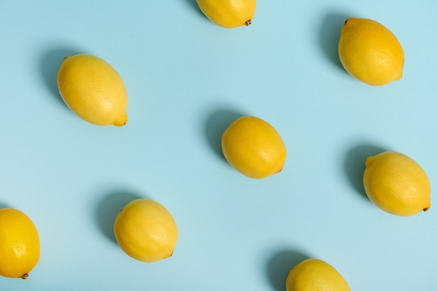 파란색 파스텔 표면에 패턴으로 배치된 익은 노란색 밝은 레몬과 함께 창의적인 여름 음식의 미니멀한 배경을 볼 수 있습니다. 평평한 평지, 광고를 위한 복사 공간. 부드러운 빛으로 촬영한 스튜디오