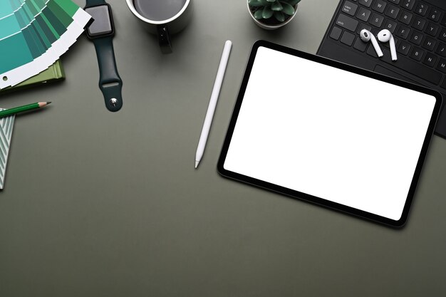 Photo top view of creative workplace with smart watch, mobile phone , wireless keyboard, color swatches, earphone and copy space on green table.