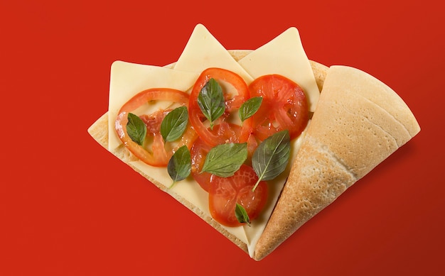 TOP VIEW OF CREPE OR FINE PANCAKE marguerita flavor with slices of tomato, basil, cheese ON A RED BACKGROUND.