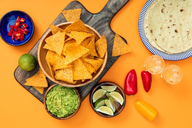 Top view of crispy Mexican nachos served on wooden cutting board with guacamole peppers limes