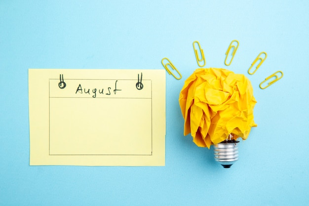 Foto carta stropicciata vista dall'alto con carta promemoria idea concetto lampadina per agosto su sfondo blu