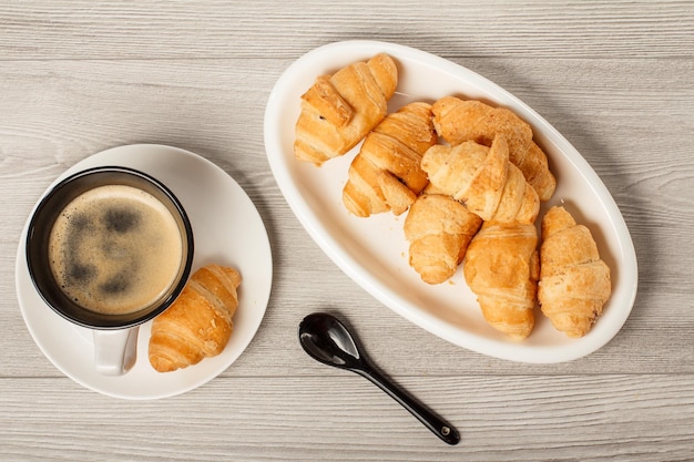 Top view of cup of black coffee and fresh croissants on white porcelain dish