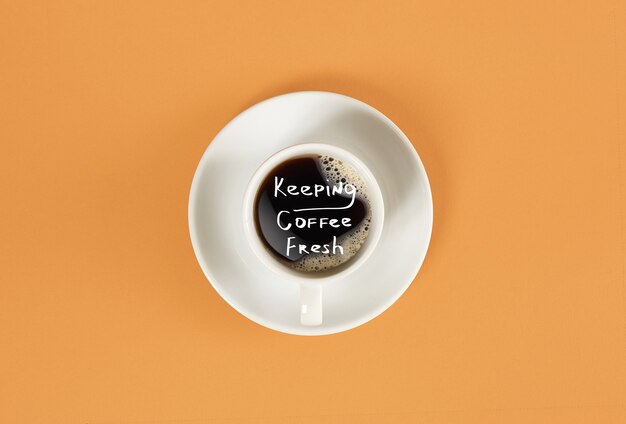 Top view of cup of black coffee and keeping coffee fresh lettering isolated on orange background