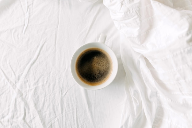 Вид сверху чашки черного кофе на белой простыне Завтрак в постели концепции