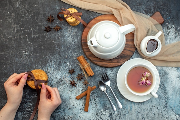 Top view of a cup of black tea and kettle on wooden board hand holding cookies on ice background