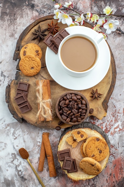 top view cup of coffee cookies bowl with coffee beans chocolate cinnamon sticks tied with rope anise stars on rustic wood board on table