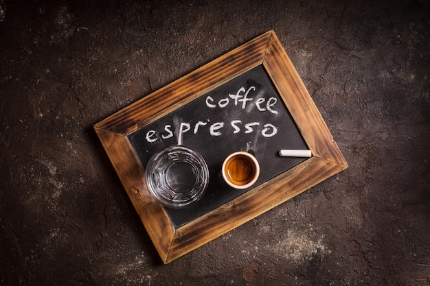 Vista dall'alto di una tazza di caffè e acqua di vetro su una lavagna vecchia scuola con iscrizione