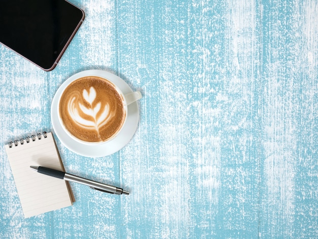 Top view of a cup of coffee, notebook and smartphone on blue wooden table background
