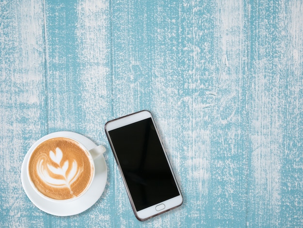 Top view of a cup of coffee and white smart phone on blue wooden table background