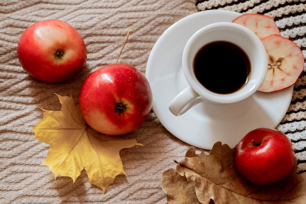 Top view on cup of espresso coffee on plaid surrounding with yellowed autumn leaves and red apples