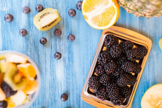 Вид сверху на чашку, полную вкусных фруктов над деревянным столом. Ягода, банан, киви и виноград на синем столе