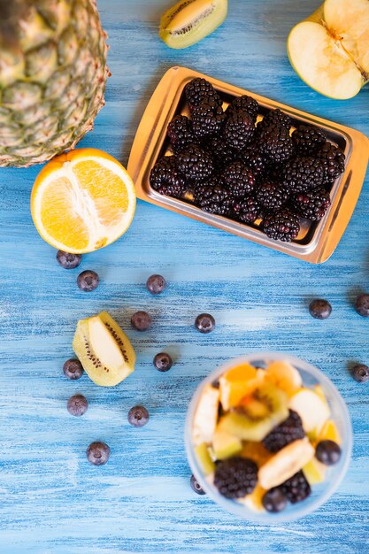 Top view of a cup full of tasty fruits in a cup . Berry, banana orange on wooden table