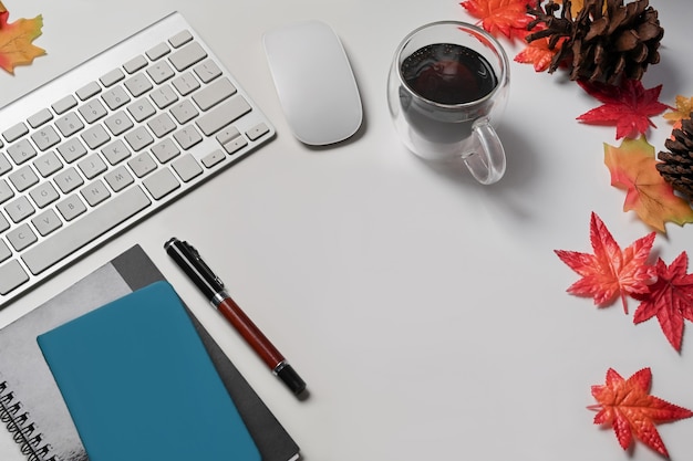 Top view cup of hot beverage, notebooks and autumn maple leaves on white background.