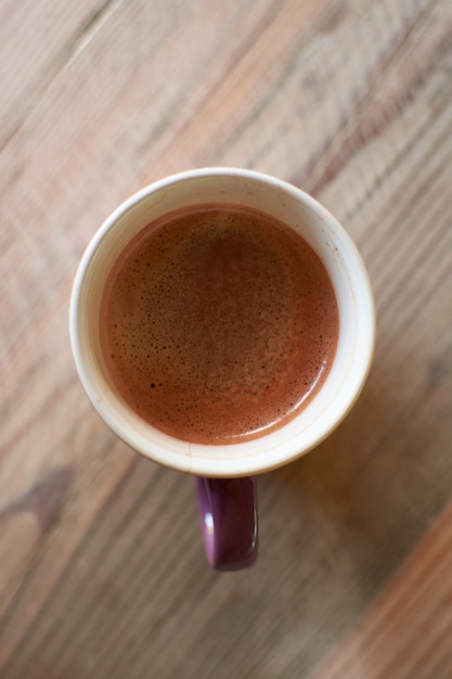 A top view of a cup of hot coffee on a wooden table