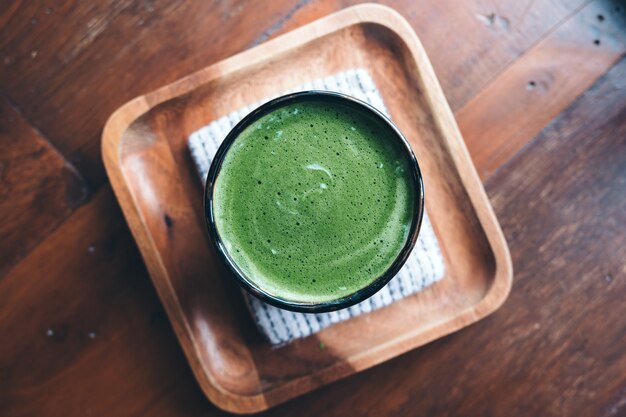 Photo top view of a cup of hot matcha latte on wooden floor