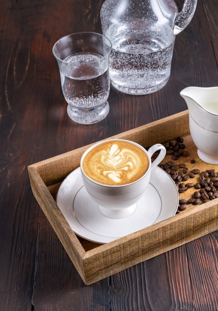 Vista dall'alto una tazza di caffè latte art, acqua e chicchi di caffè in una scatola di legno al buio