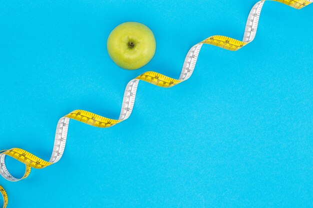 top view of curved measuring tape and apple isolated on blue