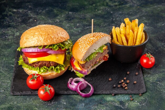 Top view of cut whole delicious sandwiches and tomatoes with stem onions fries on black tray on dark surface