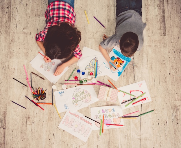 Top view of cute children drawing while lying on the floor.