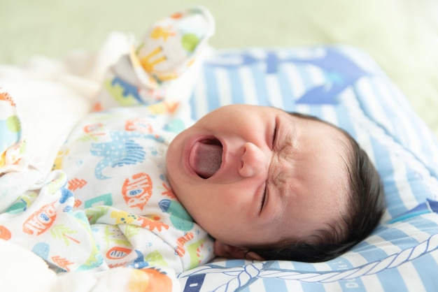 Vista dall'alto di una graziosa bambina asiatica sdraiata sul letto e che piange