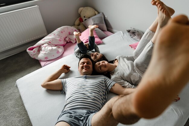 Top view of a cute little girl and her beautiful young parents looking at the camera and smiling, lying on the floor at home,Vvew from above of resting family lying on the floor and looking at camera